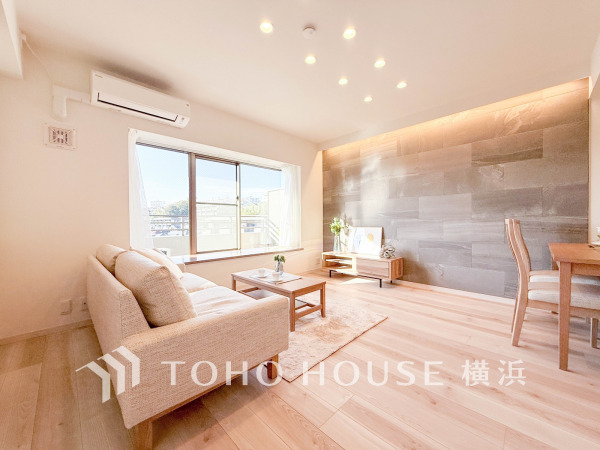 自然光がたっぷり入る明るいリビング。落ち着いたアクセントウォールと木の温もりが調和した空間です。