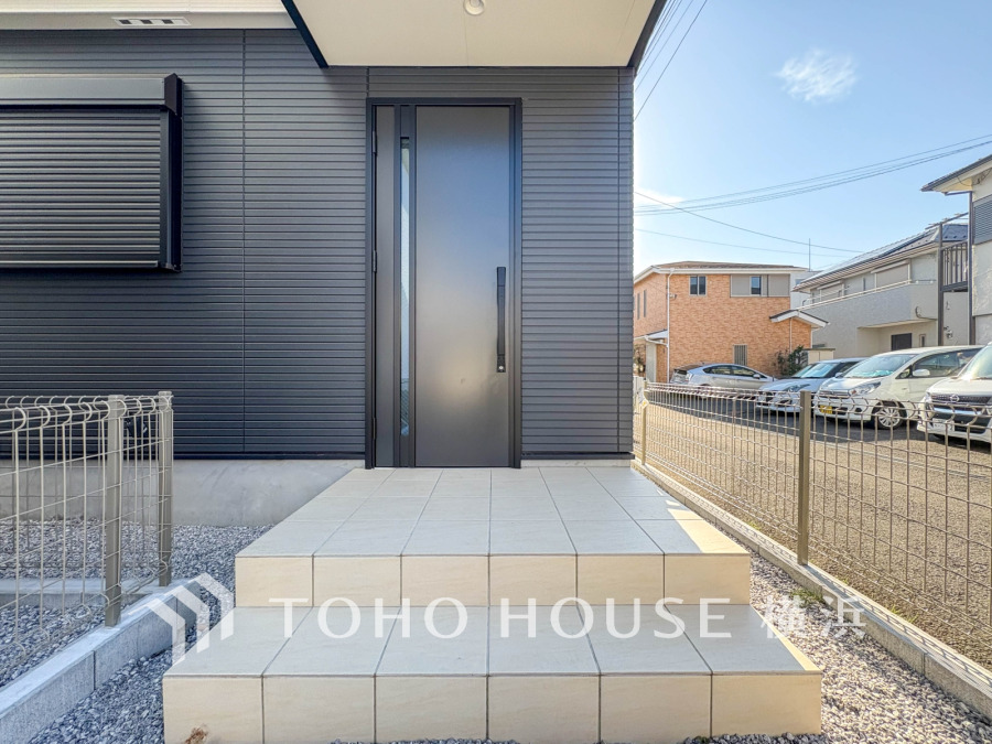 シンプルでスタイリッシュな玄関ドアと広々としたタイル貼りのアプローチが魅力の住まい外観です。