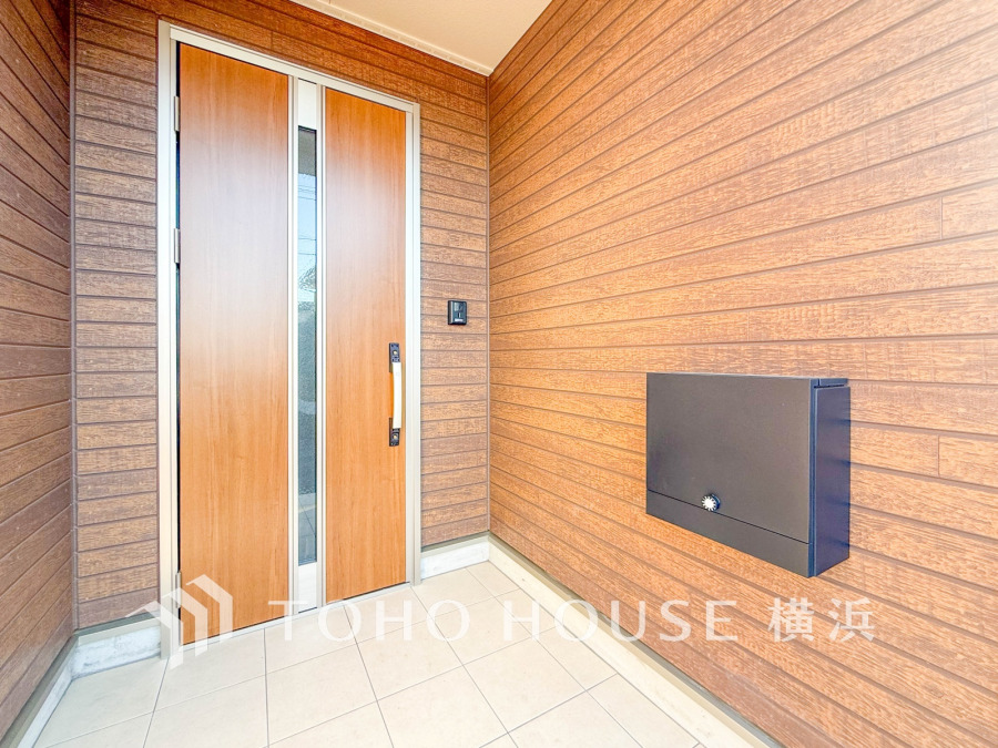 木目調の温かみある玄関扉と広々としたタイル張りのポーチが、上質で落ち着いた印象を演出します。