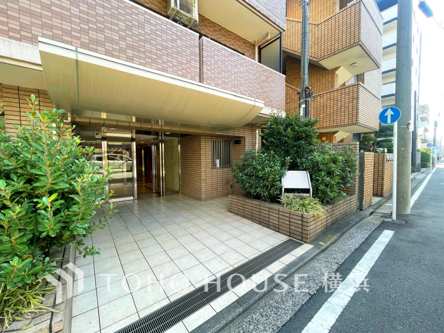 落ち着いたタイル貼りの外観と緑豊かな植栽が調和した、清潔感あふれるマンションのエントランスです。