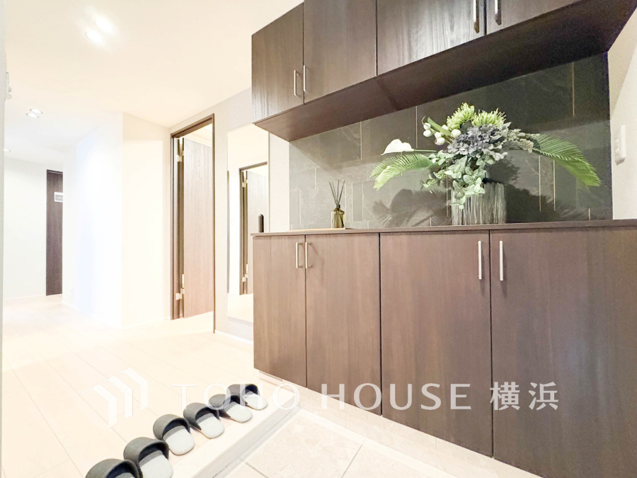 落ち着いた木目調の収納と大きな鏡が設置された広々とした玄関スペースです。