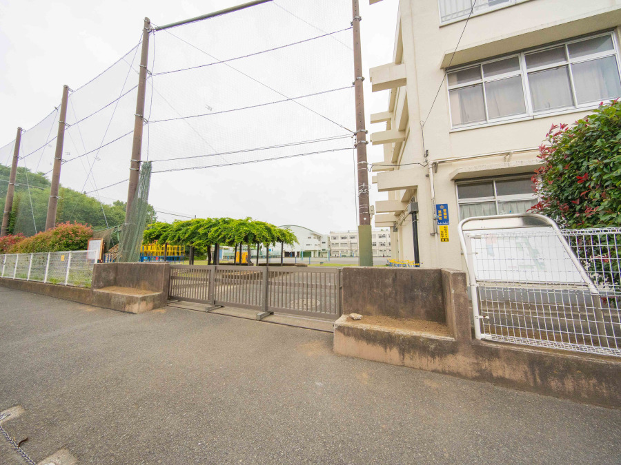 緑豊かな環境に囲まれた学校の正門。広々とした校庭と遊具が見え、子どもたちの安全を守るネットも完備しています。
