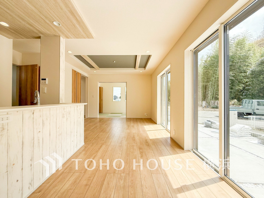 大きな窓から陽光が差し込む明るいリビング。木目調の温かみある空間は上質な家族の憩いのスペース。