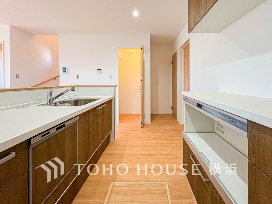 木目調の収納と白いカウンターが調和する、使いやすさと清潔感を兼ね備えたシステムキッチンです。