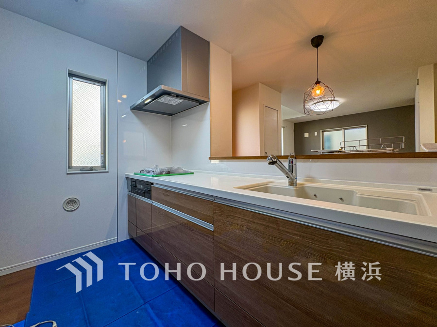 木目調の収納と白いカウンターが調和する、開放感ある対面キッチン。自然光が差し込む明るい空間です。