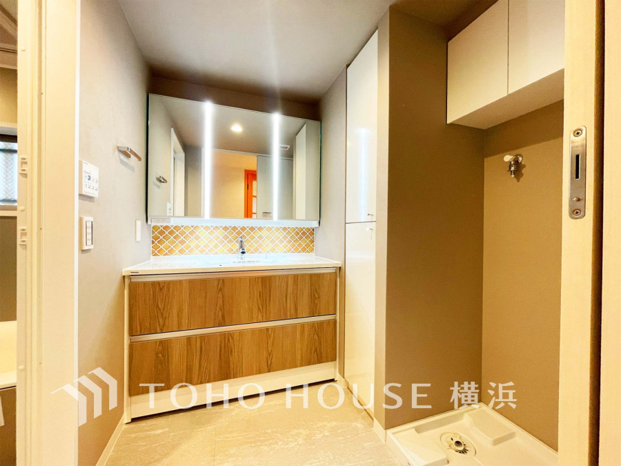 木目調の洗面台と収納が調和する、明るく機能的な洗面スペース。洗濯機置き場も完備しています。