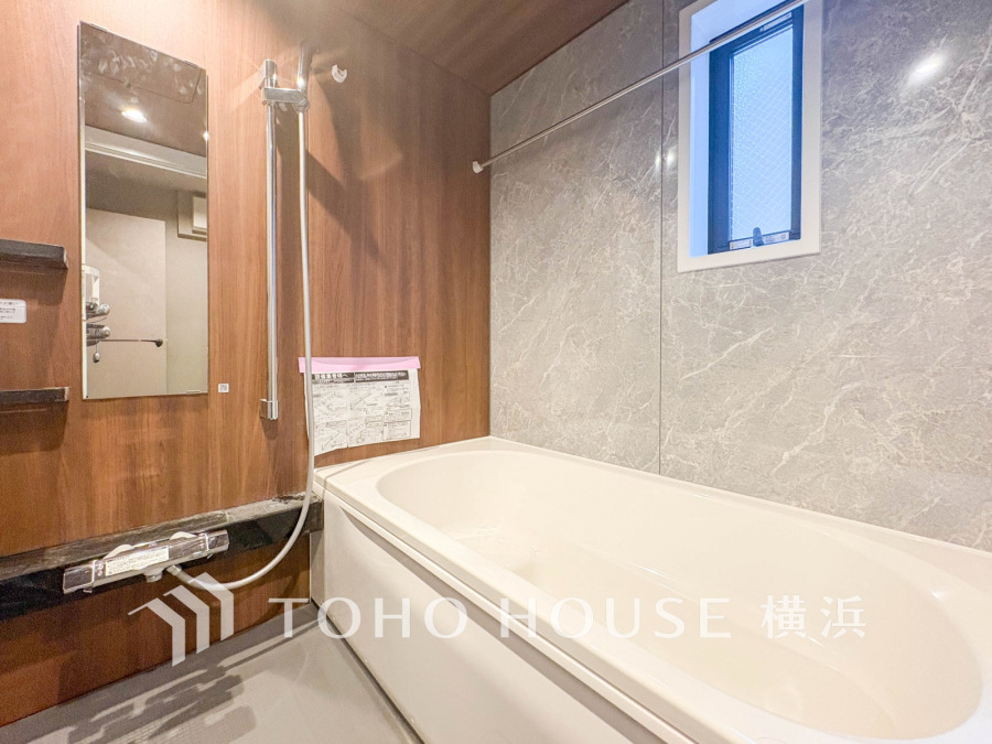 木目調パネルと大理石調壁が調和する、落ち着いた雰囲気のバスルーム。窓で換気も快適です。