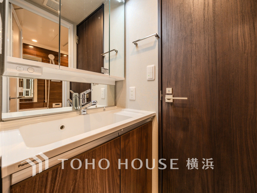 木目調の扉と清潔感ある洗面台が調和した、機能的で落ち着いた雰囲気の洗面スペースです。