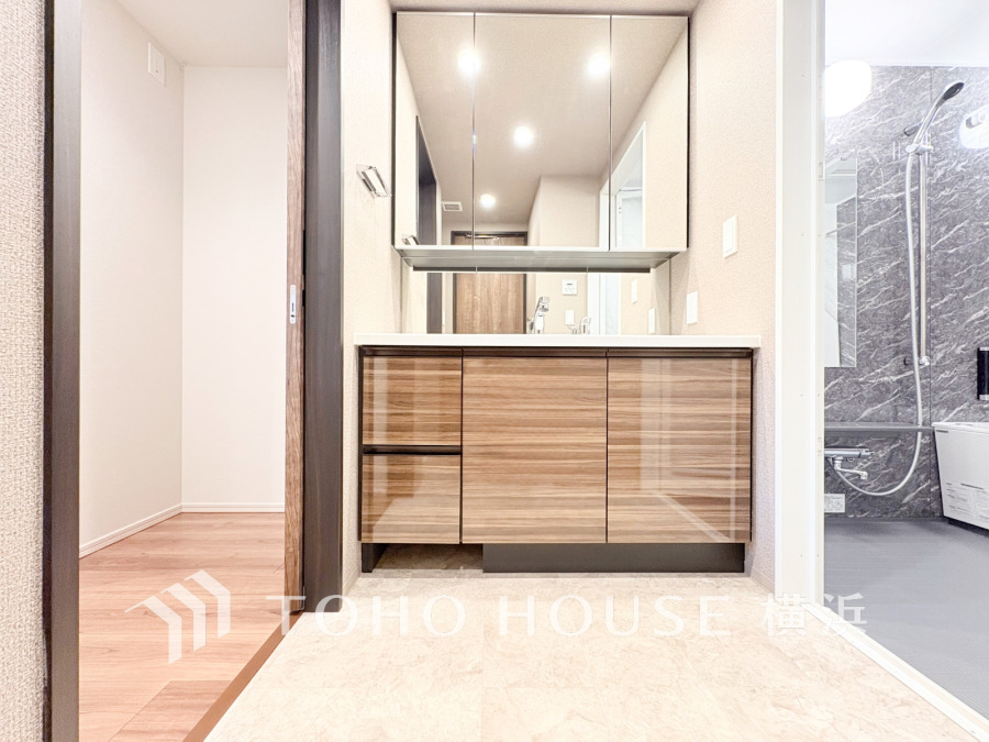 木目調の収納と大きな鏡が特徴の洗面台。隣接する浴室もシックなデザインで統一感があります。