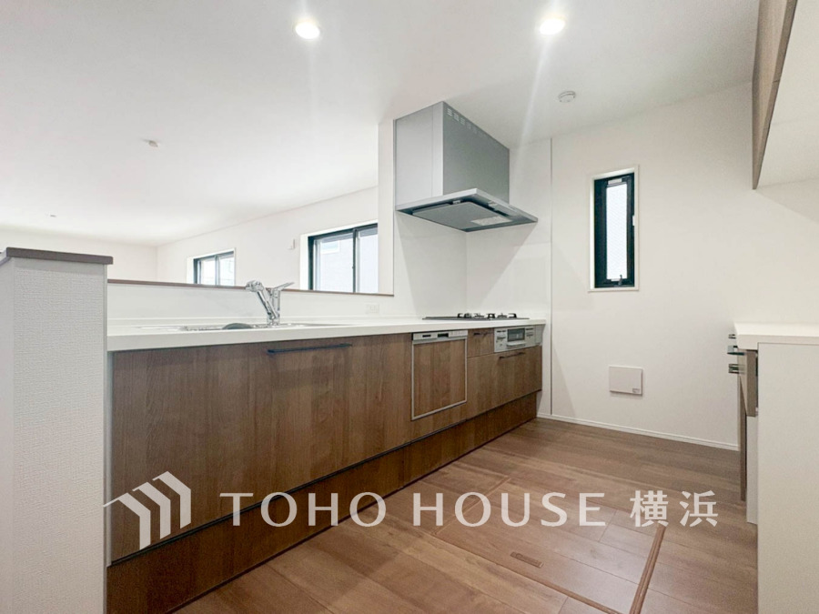 木目調の収納と白い天板が調和する、明るく開放的な対面キッチン。家族との会話も楽しめる設計です。