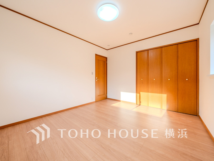 温かみある木目調の床と収納扉が調和する、明るい洋室。