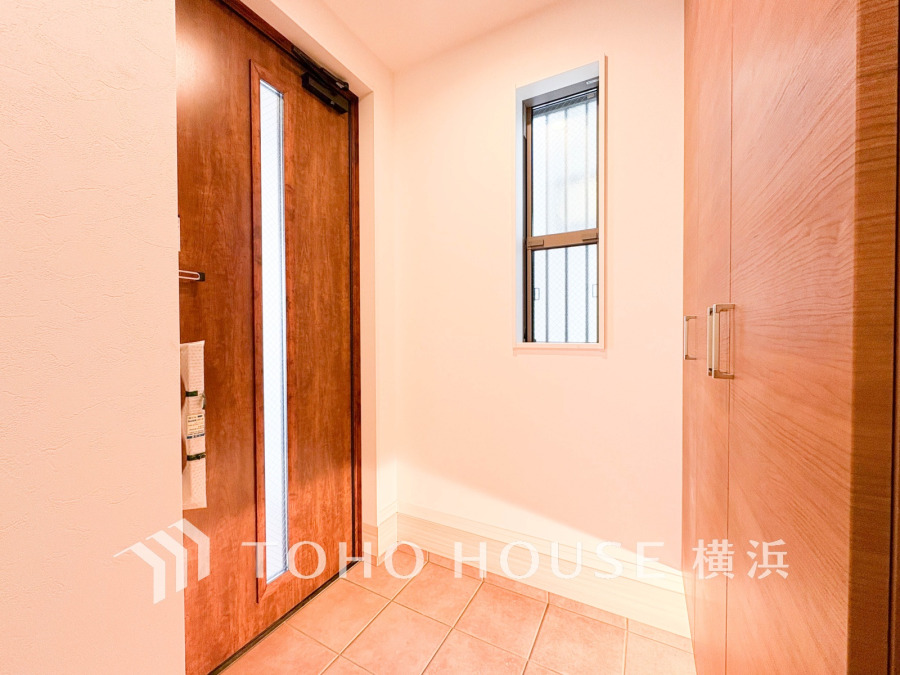 温かみのある木目調ドアと収納が調和する玄関スペース。明るい窓から自然光が差し込み、清潔感あふれる空間です。