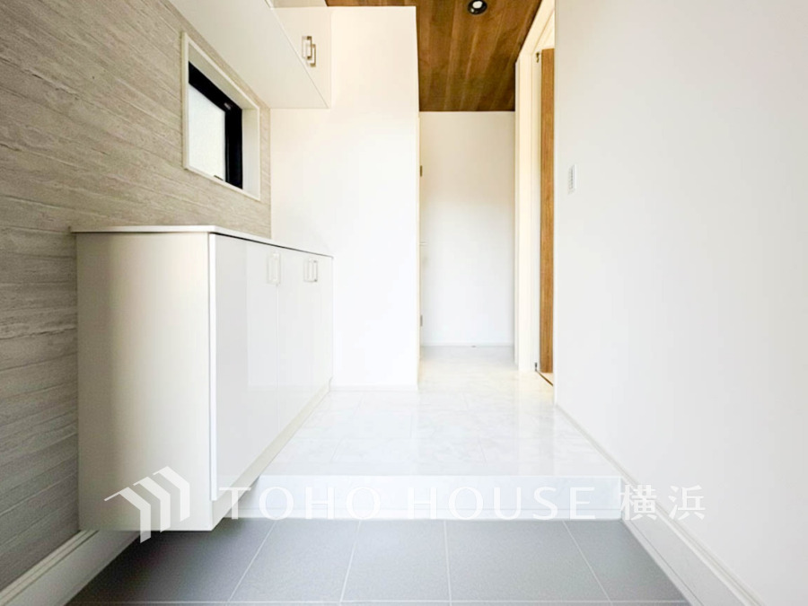 清潔感あふれる白基調の玄関。壁掛け収納でスッキリ収納、木目天井が温かみをプラスしています。