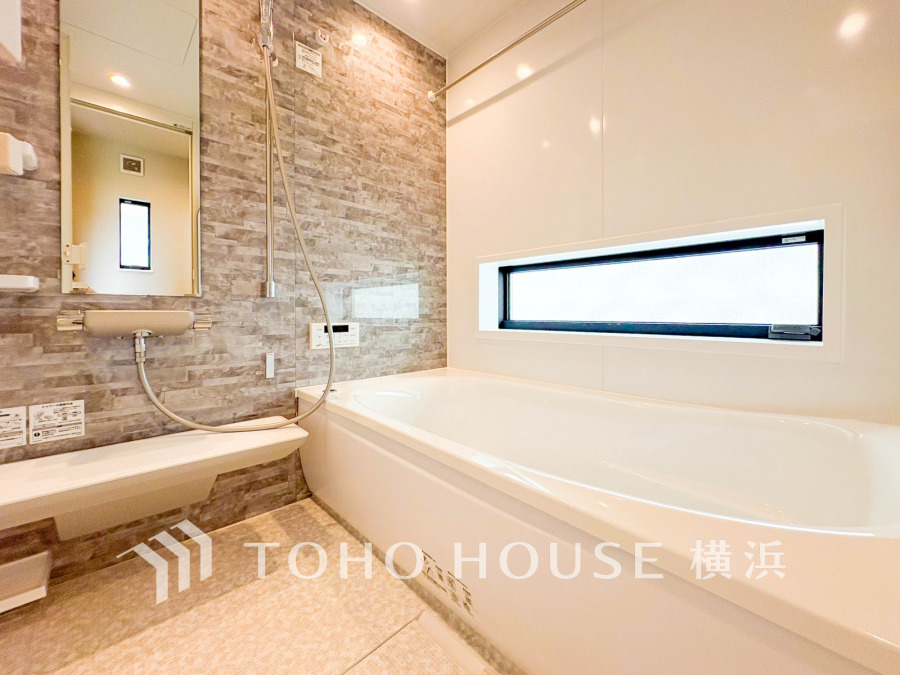 落ち着いたタイル調の壁と横長窓が特徴の、明るく開放感のある清潔なバスルームです。