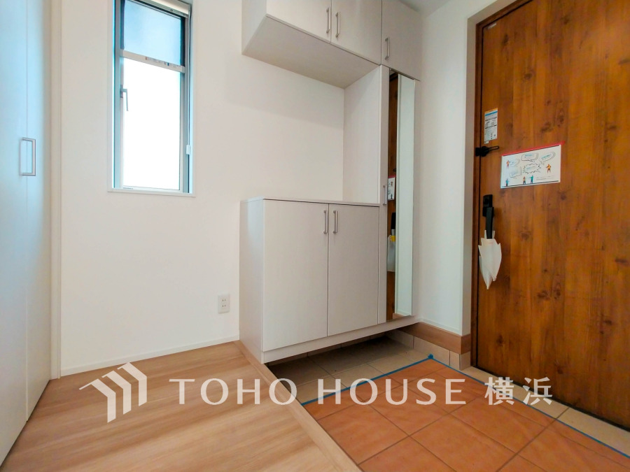 木目調の玄関ドアと白を基調とした収納が調和する、明るく清潔感あふれる玄関スペースです。