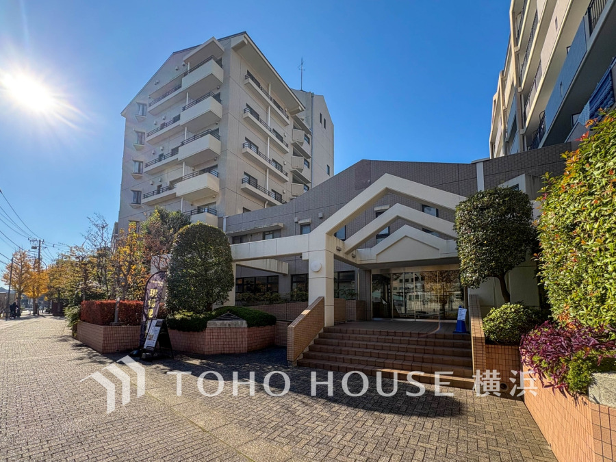 陽光降り注ぐエントランスが印象的な、緑豊かな落ち着いた住環境のマンション外観です。