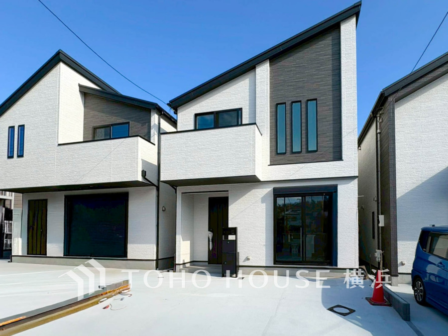 白とグレーを基調としたモダンな外観の新築一戸建て。駐車スペースも広く確保されています。