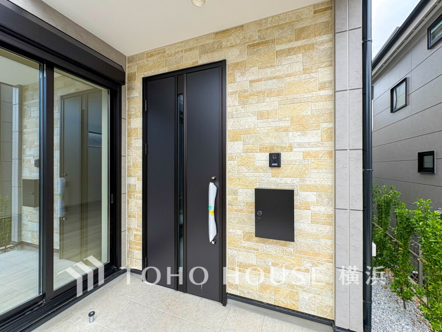 スタイリッシュなブラックドアと温かみのあるタイル壁が調和した、落ち着きのある玄関ポーチ空間です。