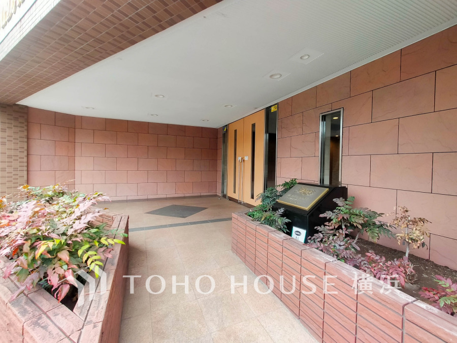 落ち着いた色合いのタイル壁と植栽が調和する、上品なエントランスです。