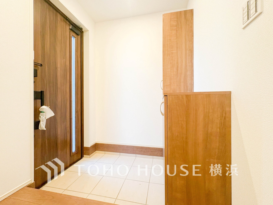 木目調の玄関ドアと収納が調和する、明るく清潔感あふれる広々とした玄関スペースです。