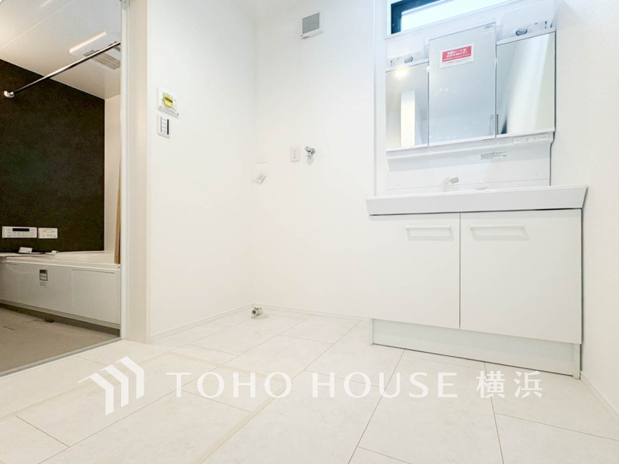 清潔感あふれる白基調の洗面所。隣接する浴室は落ち着いたダークカラーでメリハリのある空間です。