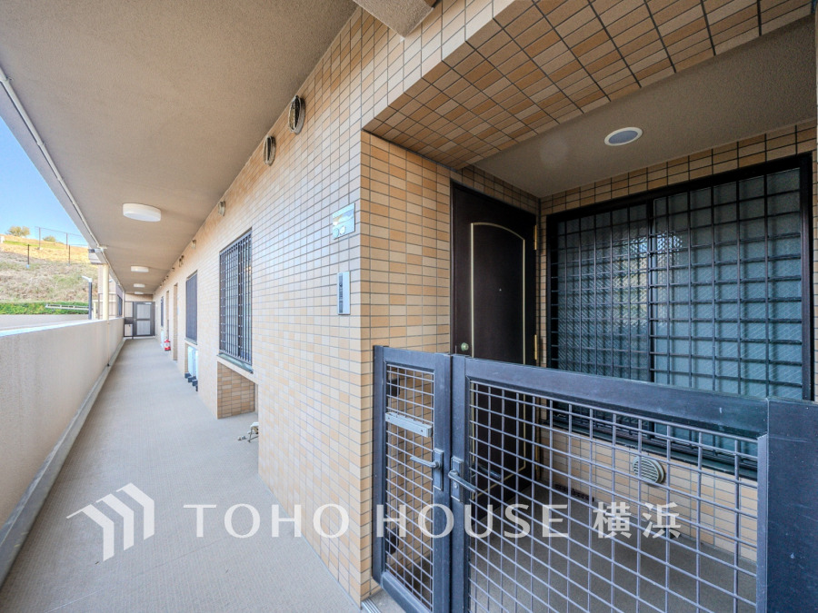 タイル張りの外壁と広々とした共用廊下、プライベート感のある門扉付き玄関が魅力のマンションエントランスです。