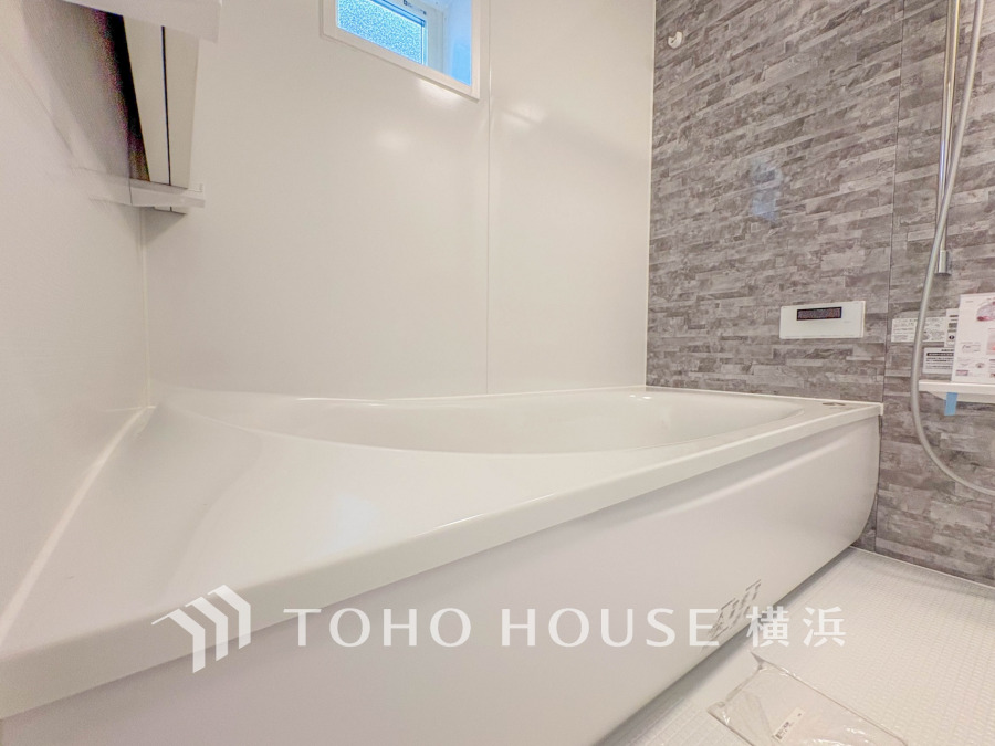 清潔感あふれる白を基調とした浴室は、モダンなグレーのアクセント壁で落ち着いた空間を演出しています。