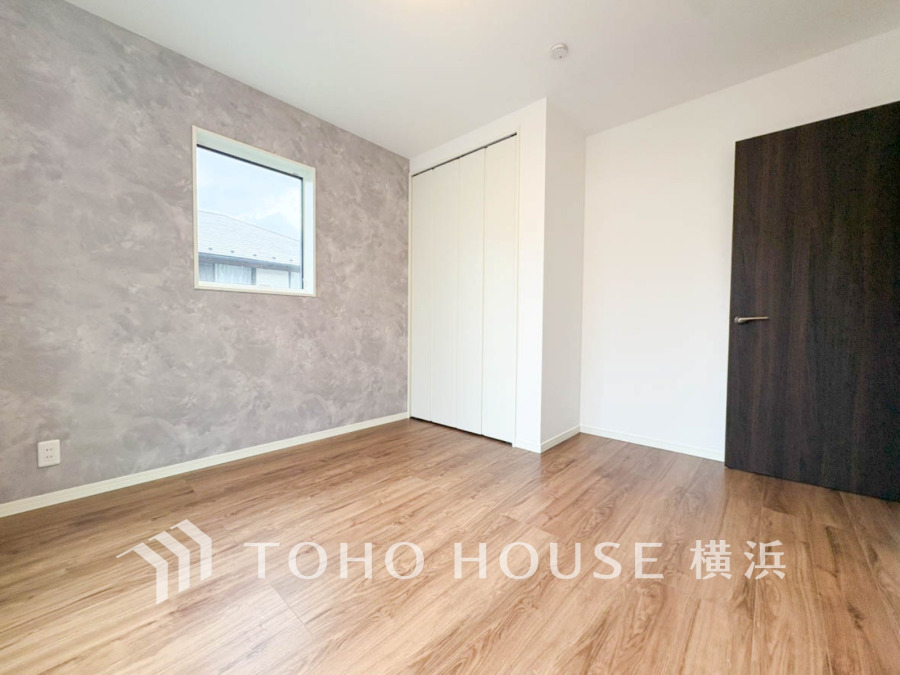 落ち着いたグレーのアクセントクロスと木目調フローリングが調和する、明るくゆとりある洋室です。