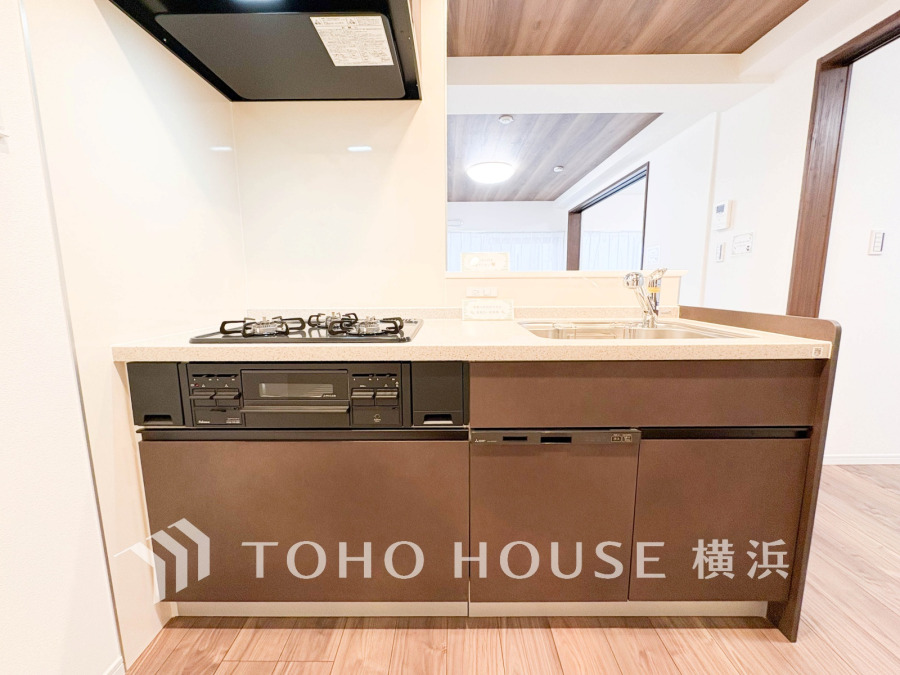 落ち着いたブラウンのシステムキッチン。3口ガスコンロと食器洗浄機付きで快適な調理環境を実現しています。