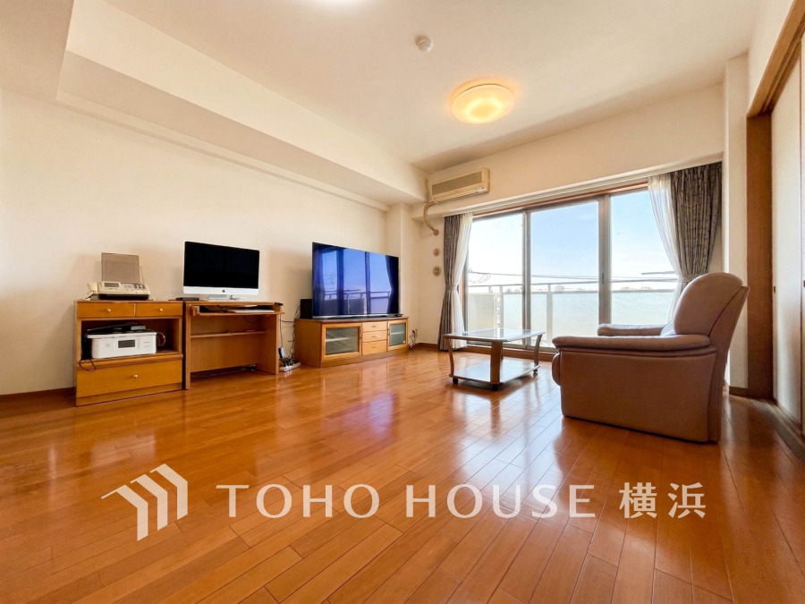 明るい陽光が差し込む広々リビング。木目調の床と家具が温かみを演出し、快適な居住空間を実現しています。