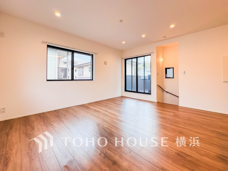 明るい窓から自然光が差し込む、広々とした木目調のフローリングが美しいリビングルームです。