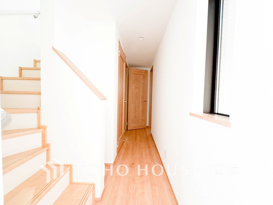 明るい自然光が差し込む、清潔感あふれる廊下と木目調の階段が調和した住まいの一角です。