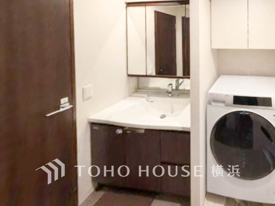 洗濯機と収納付きの洗面台を備えた機能的な洗面室。落ち着いた色合いで清潔感があります。