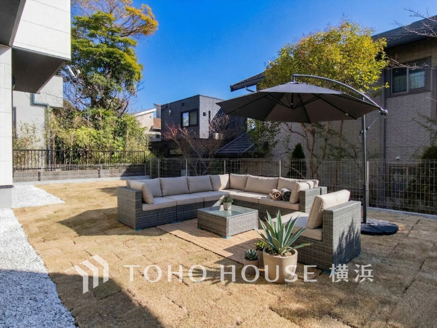 日差しあふれる広い庭にゆったりくつろげるソファセットを配置した、開放感のあるアウトドアリビング空間です。（装飾品はAI家具です）