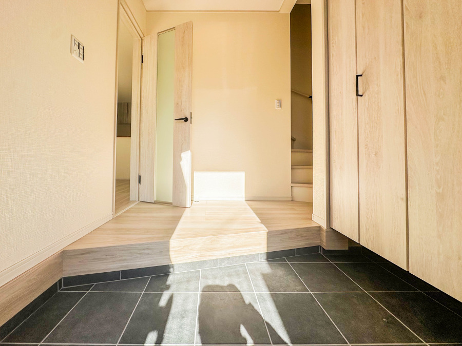 明るい光が差し込む広々とした玄関。木目調の収納と落ち着いたタイルで上質な印象です。