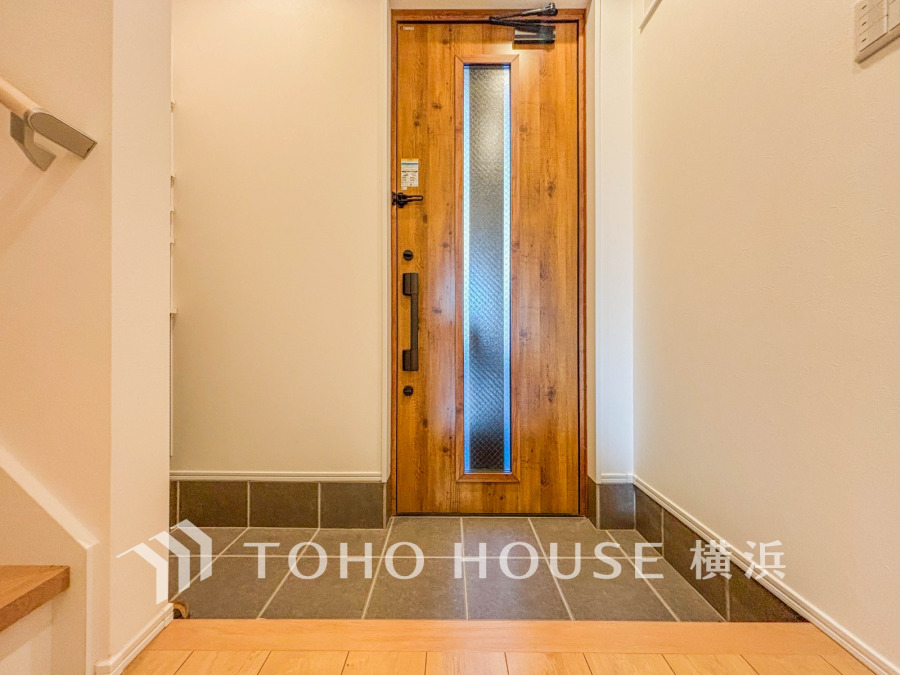 温かみのある木製ドアと落ち着いたタイル床が迎える、清潔感あふれる広々とした玄関スペースです。