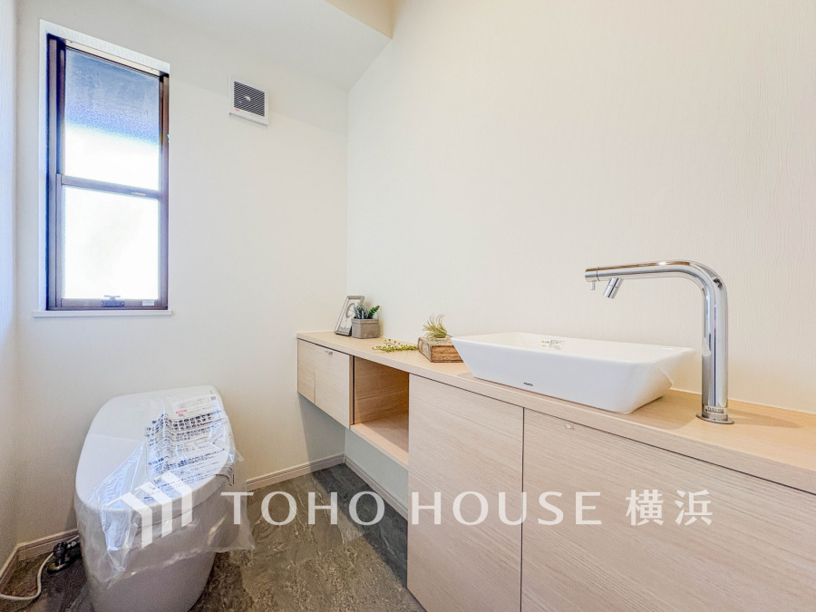 ナチュラルな木目調の収納と清潔感ある洗面台を備えた、明るく快適なトイレ空間です。