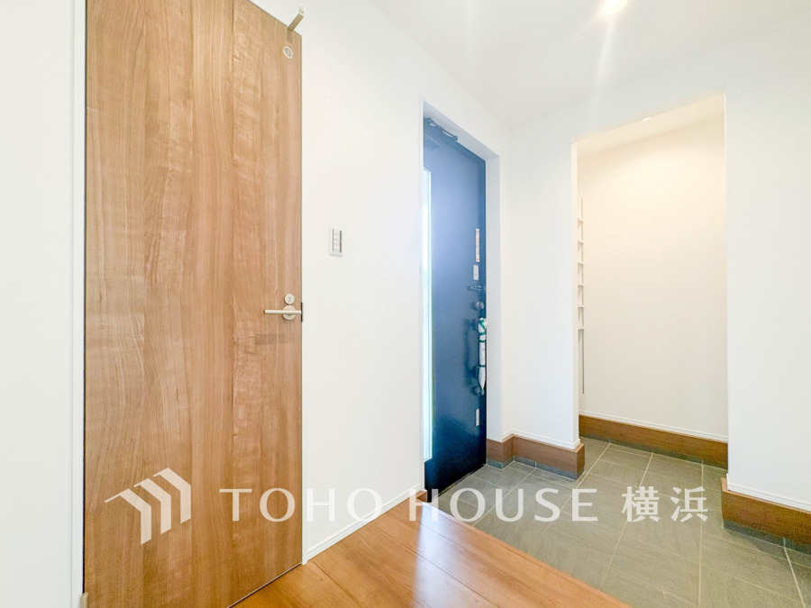 清潔感あふれる玄関ホール。タイル床と木目調ドアのコントラストが美しく、収納スペースも確保しています。