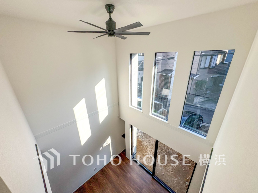 大きな窓から光が差し込む開放的な吹き抜けリビング。シーリングファンが空間の快適さを演出します。