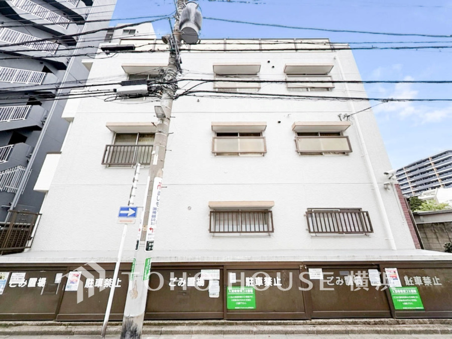 白を基調としたシンプルな外観のマンション。周囲に高層建物が立ち並ぶ利便性の高い立地です。