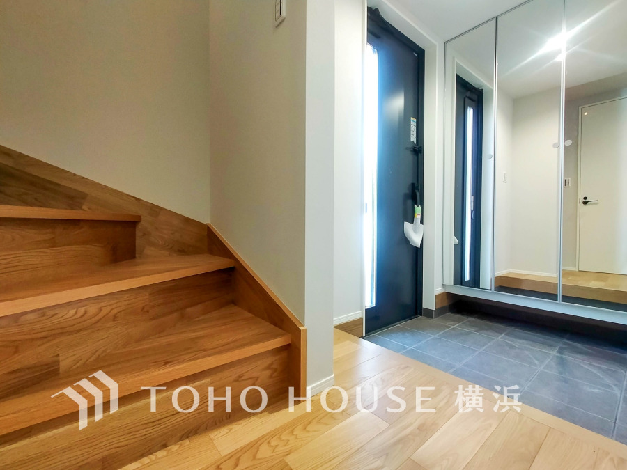 玄関は広々としたタイル張りで、壁面の大きな鏡が空間を明るく演出します。階段も木の温もりが感じられます。