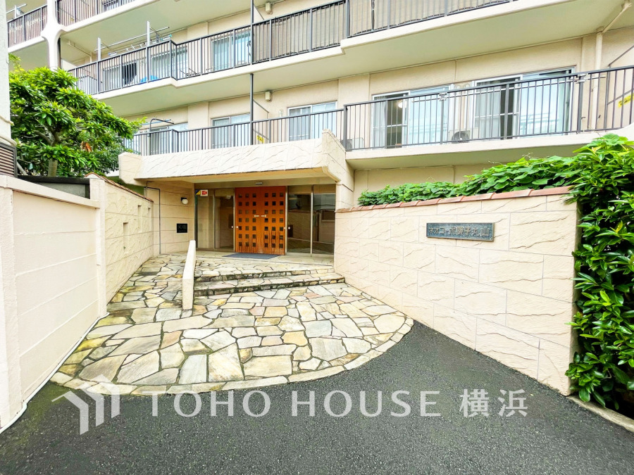緑に囲まれた落ち着いた雰囲気のマンションエントランス。上質感のあるゆったりとしたアプローチが迎えます。