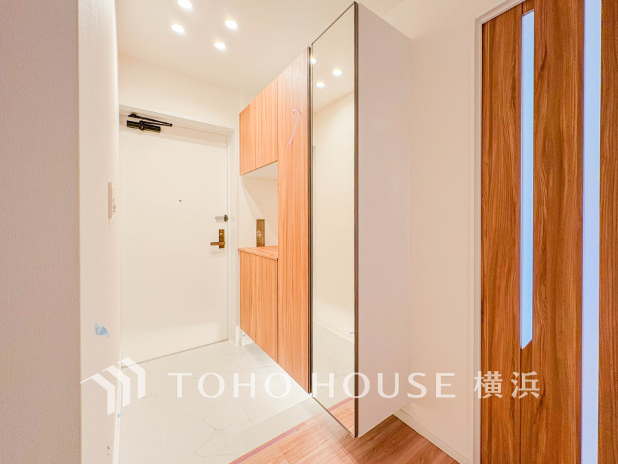 木目調の収納と大型ミラーが配された、明るく清潔感のある玄関スペースです。