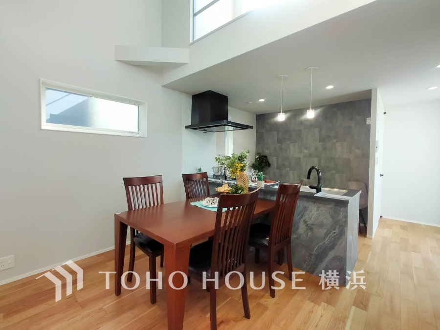 開放感ある吹き抜けと落ち着いた色調のキッチンが調和した、家族団らんに最適なダイニング空間。