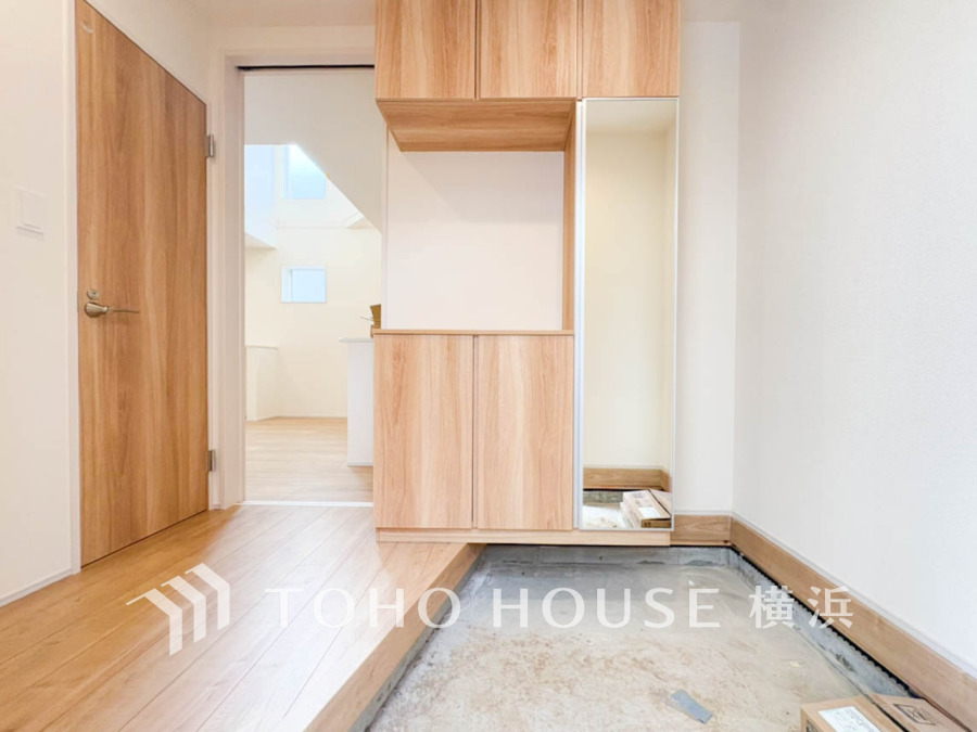 木目調の収納と鏡が備わった明るく広々とした玄関スペース。清潔感あふれる住まいの第一印象を演出します。