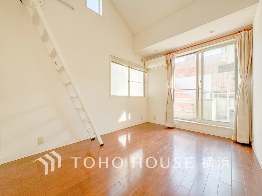 陽当たり良好な2面窓とバルコニー付きの明るい洋室。ロフトへの階段も備えた開放的な空間です。