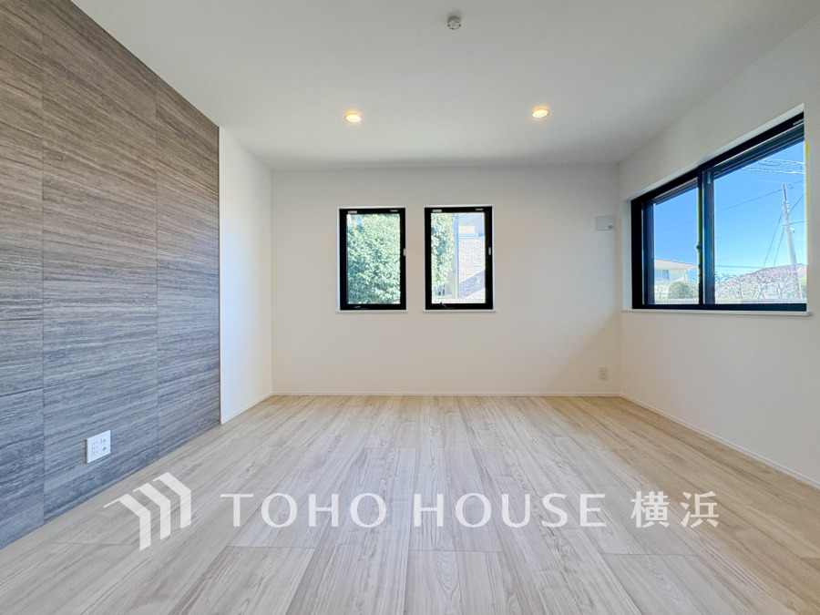 洗練されたアクセントウォールが印象的なリビング。明るい陽光が差し込み、家族の会話が弾む、心地よい団らんの時間を育みます。