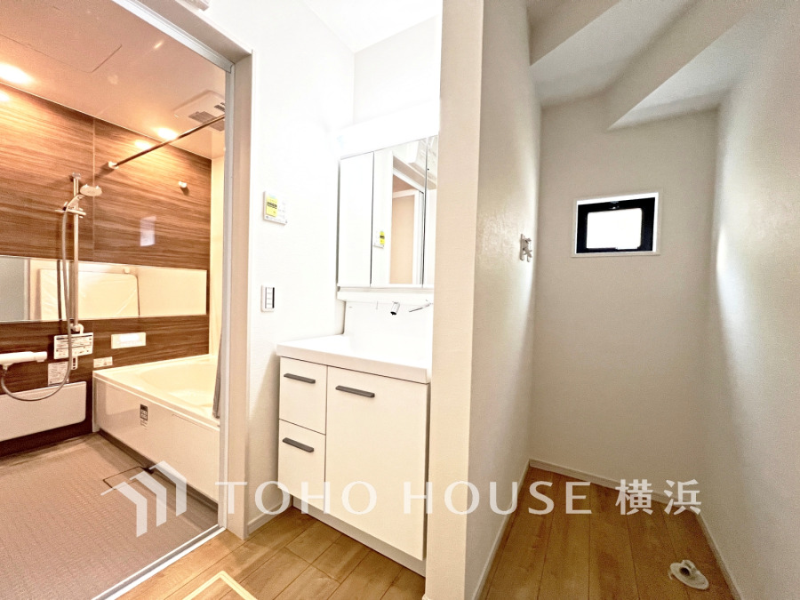 木目調の浴室と清潔感あふれる洗面台が繋がり、隣には換気窓付きの洗濯スペースを備えた実用的な水回りです。