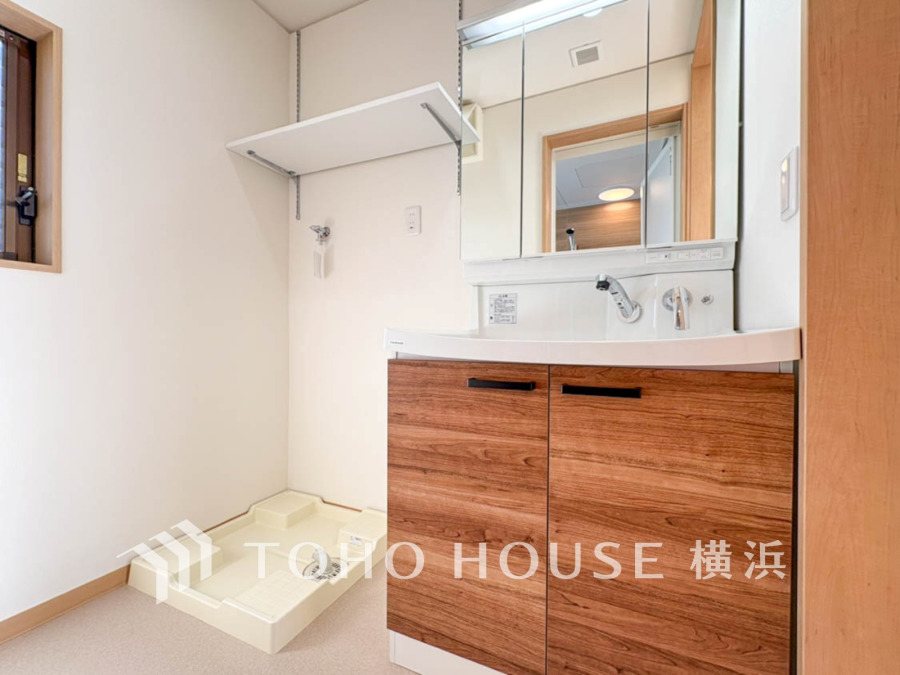 木目調キャビネットと大きな鏡を備えた洗面台と、洗濯機設置スペースが清潔感ある空間を演出します。