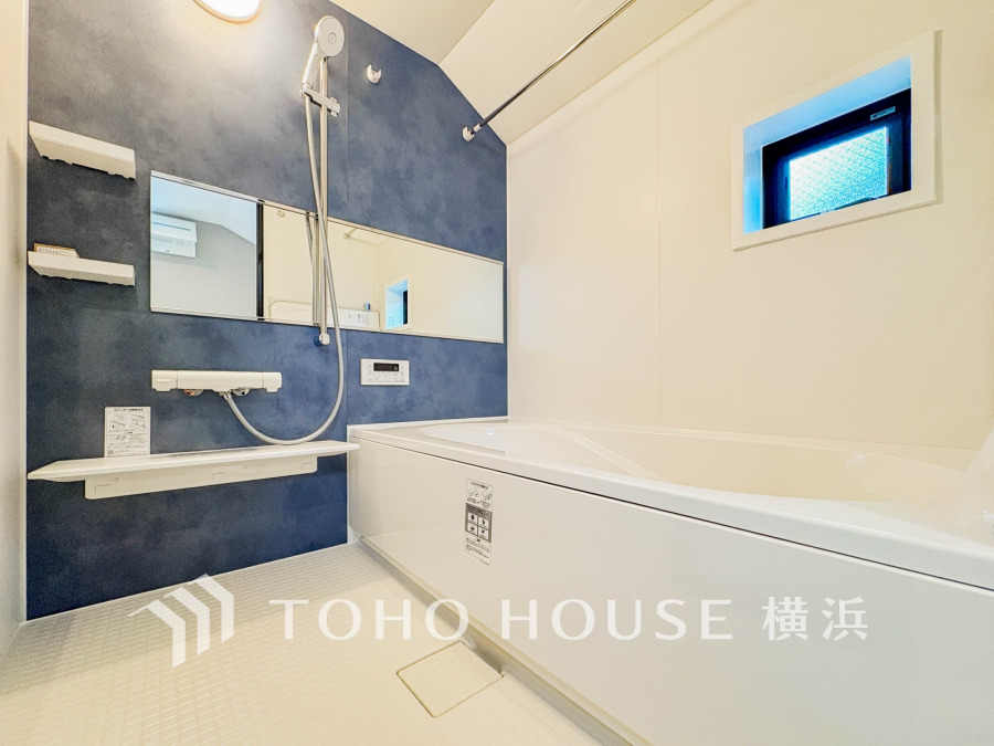 ブルーのアクセント壁が印象的な、清潔感あふれる広々としたバスルーム。小窓で自然光も取り込めます。